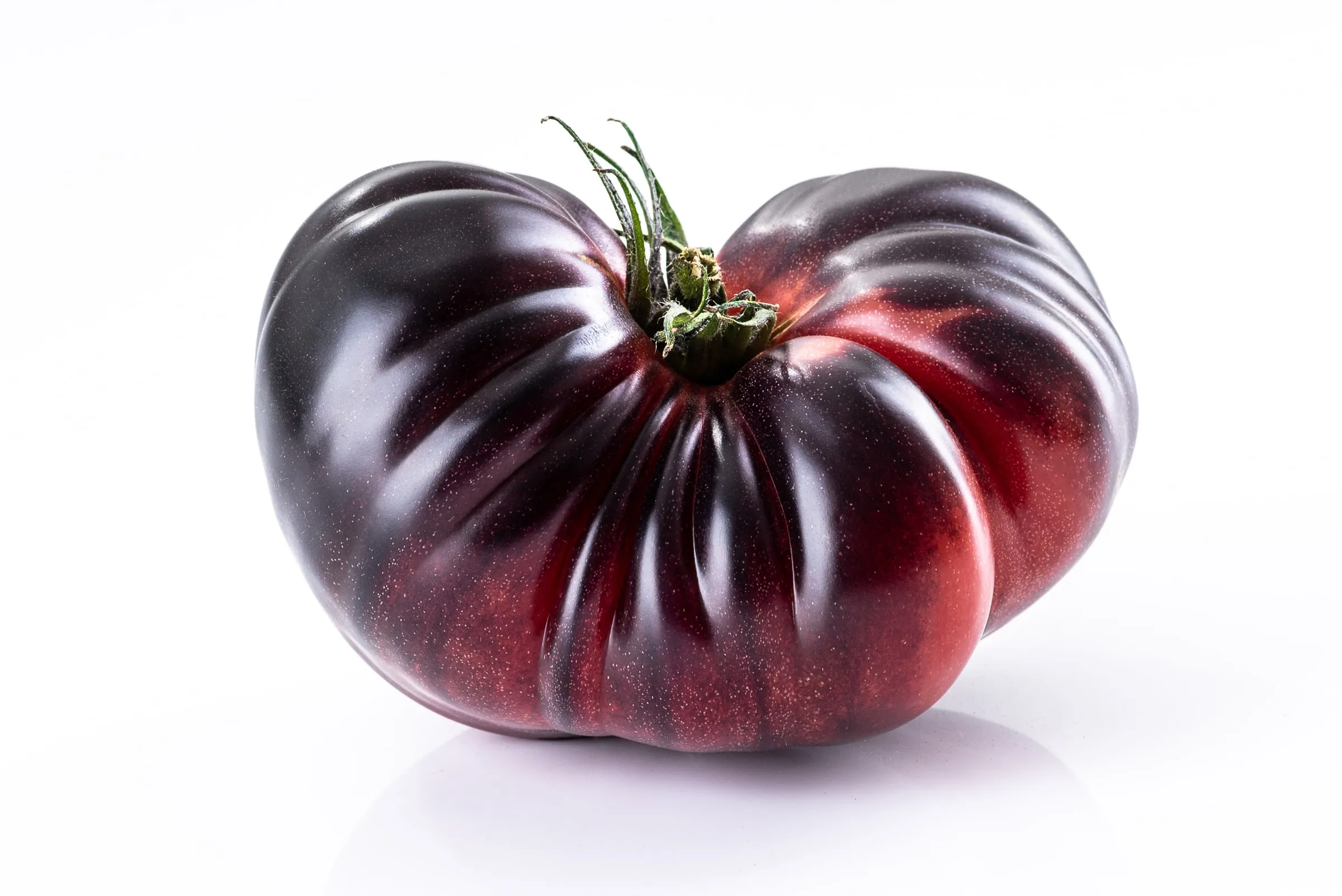 El tomate visto de perfil sobre fondo blanco, mostrando su forma acorazonada.