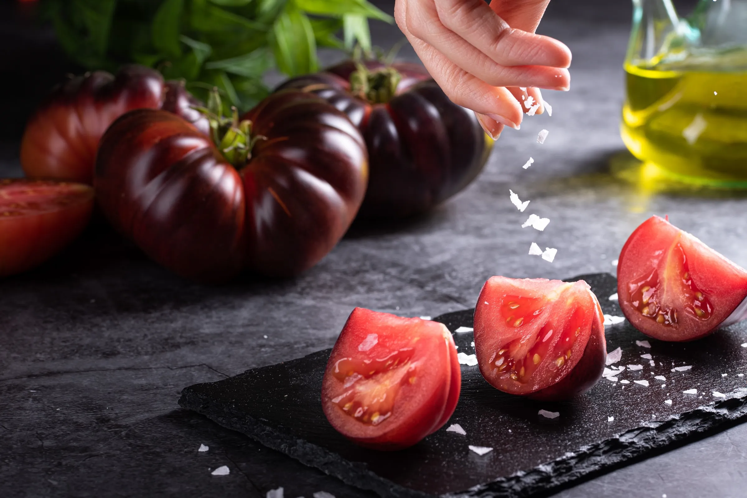 Tomates Mystika cortados y sazonados con sal en escamas, junto a tomates enteros y aceite de oliva.