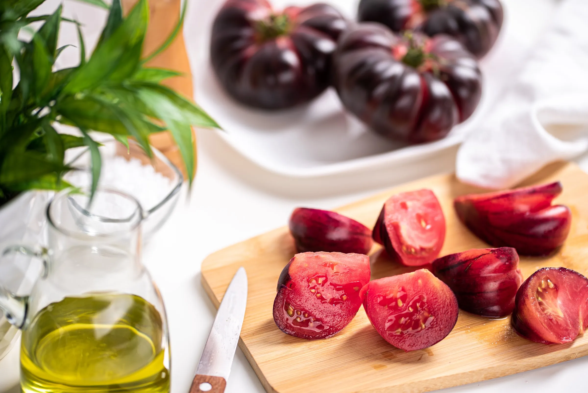 Sliced Mystika tomatoes on a wooden board, next to whole tomatoes and olive oil.